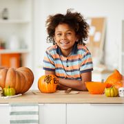 a boy  leaning on a kitchen counter surrounded by decorated pumpkins