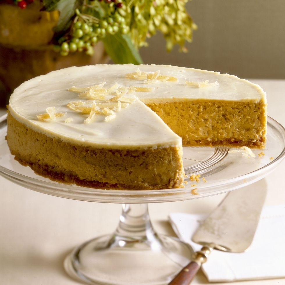 a round pumpkin cheesecake with icing on top and served on a clear cake stand