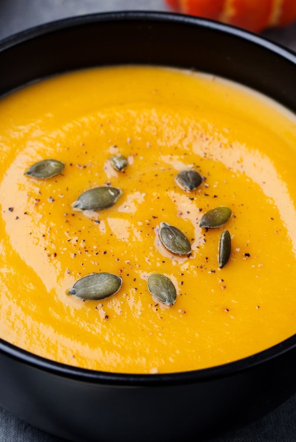 Pumpkin cream soup with pumpkin seeds in a black bowl.