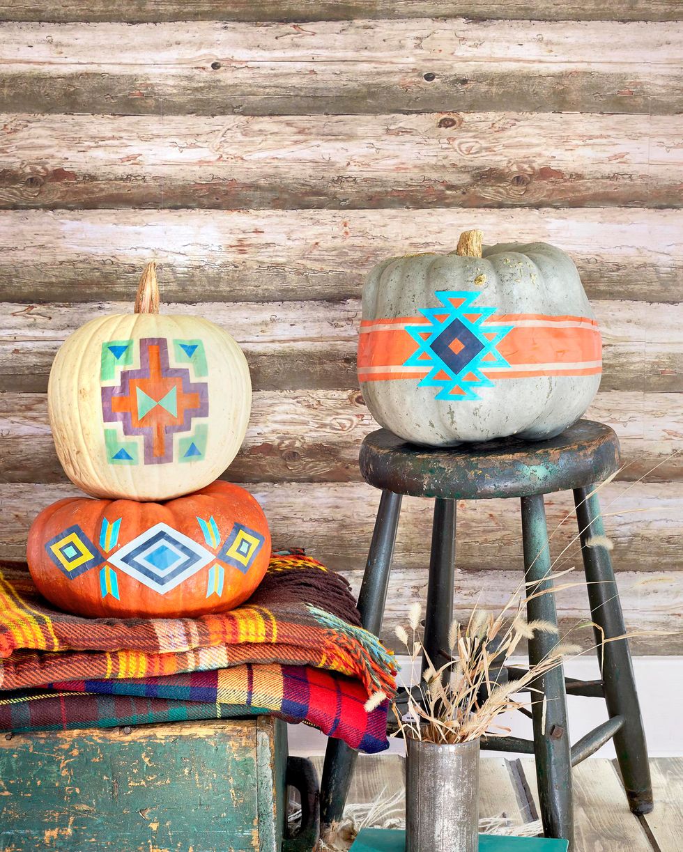 pumpkins decorated to look like pendleton blankets displayed with wool blankets, rustic chest, in front of log cabin wall