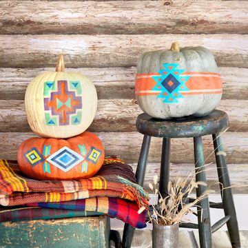 pumpkins decorated to look like pendleton blankets displayed with wool blankets, rustic chest, in front of log cabin wall