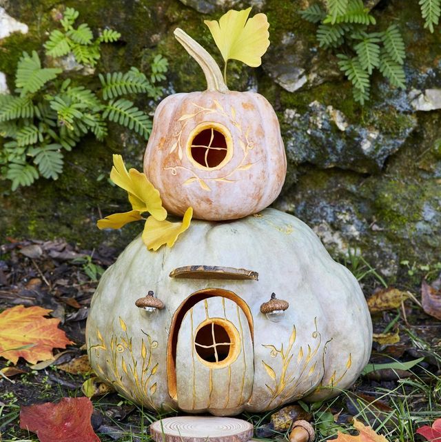 two story pumpkin fairy house with carved window and door, acorn cap porch lights, and sliced wood rounds as stepping stones