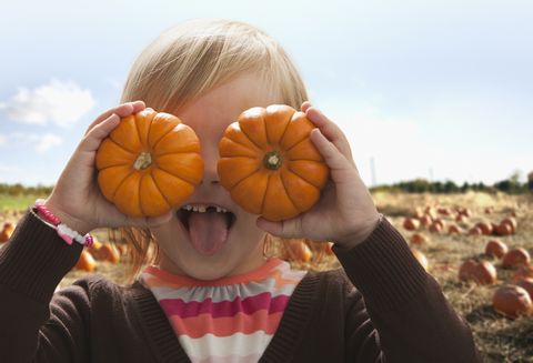caucasian girl covering eyes with small pumpkins