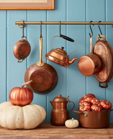 small and mini pumpkins painted copper in front of a blue painted wall with copper pots hanging from a pot rack