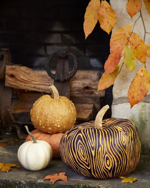 pumpkin painted dark brown with carved faux bois pattern, displayed with small pumpkins, firewood stack, and fall leaves