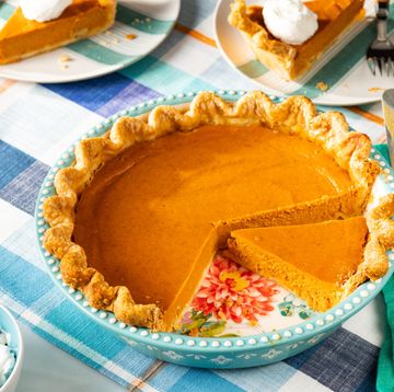 pumpkin pie recipe in a teal pie plate on a plaid table cloth with a green linen two slices of pie in the background with whipped cream
