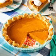 pumpkin pie recipe in a teal pie plate on a plaid table cloth with a green linen two slices of pie in the background with whipped cream