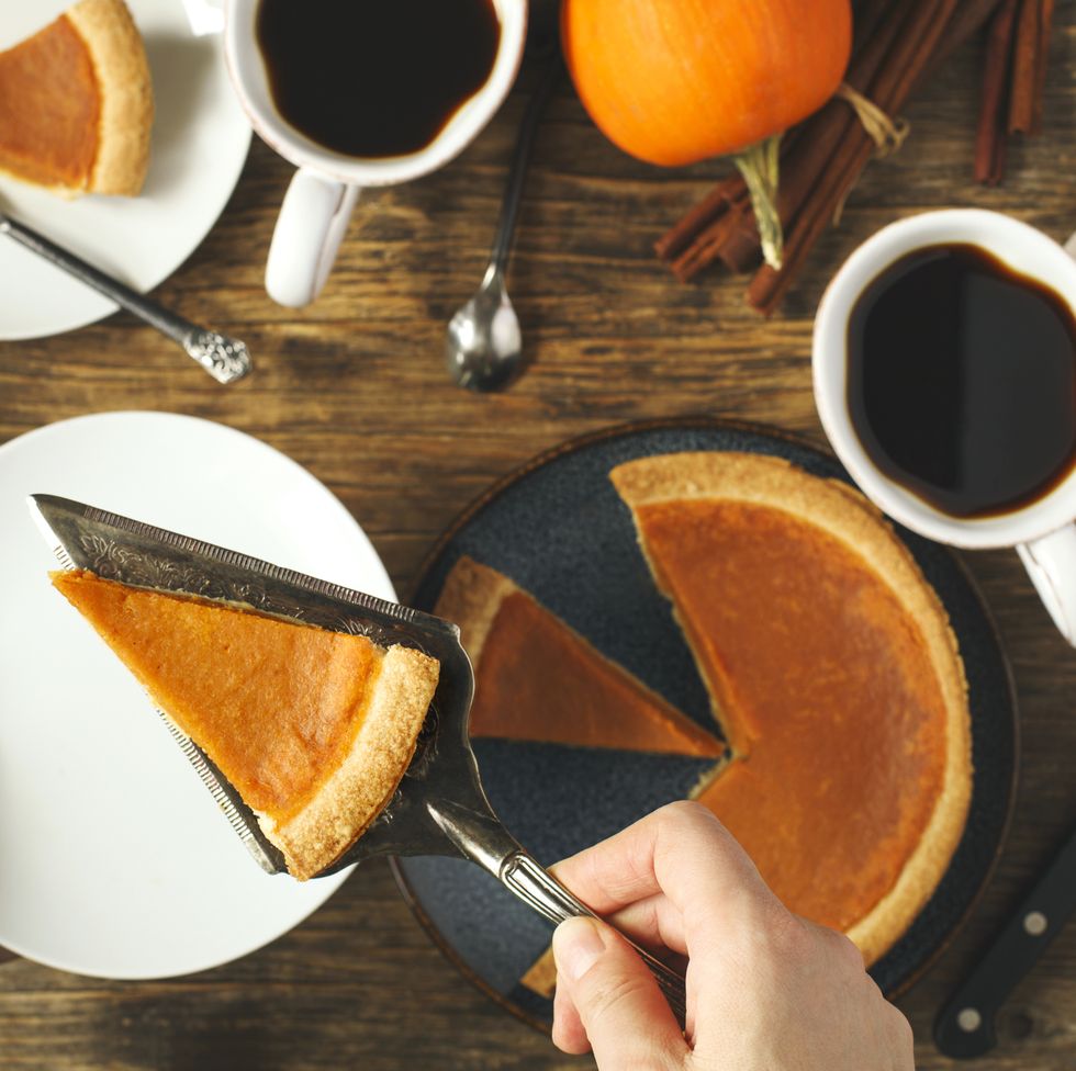 hand serving a slice of pumpkin pie with coffee cups