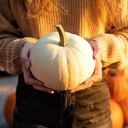 woman in orange sweater holding white pumpkin