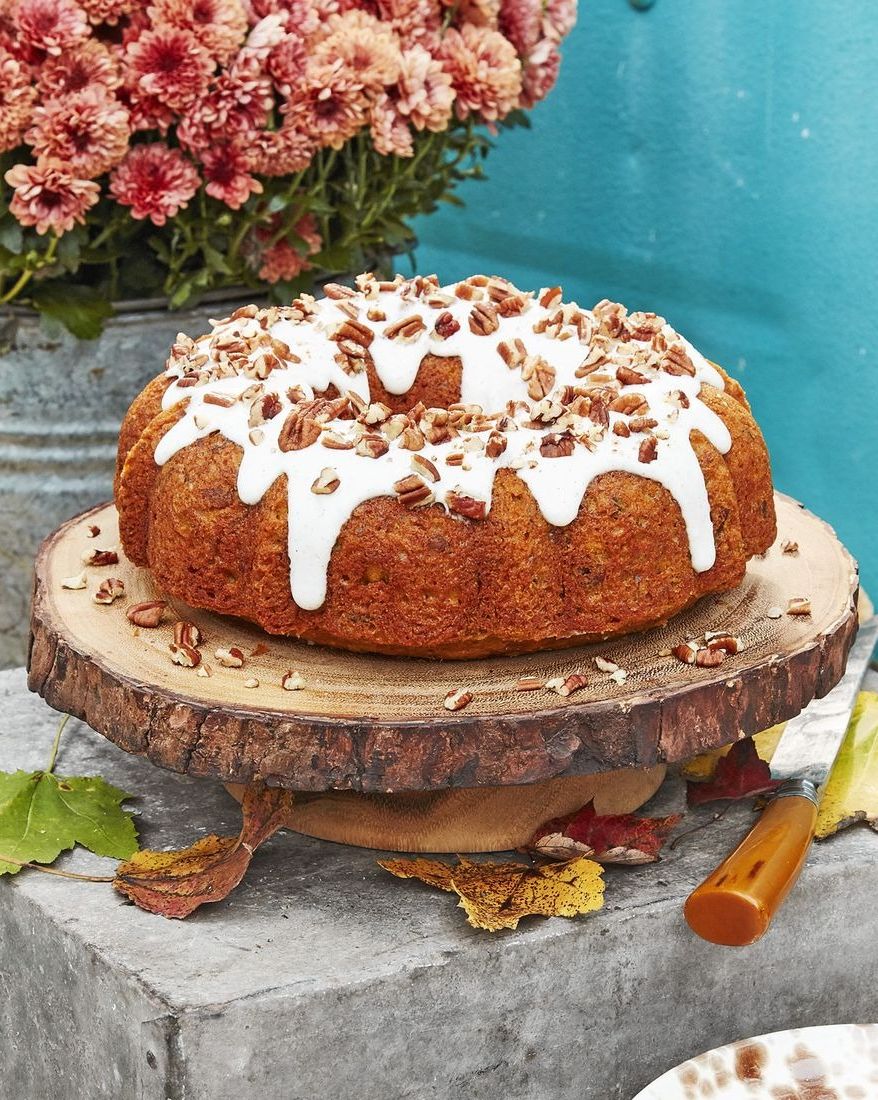 pecan pumpkin bundt cake with cream cheese glaze on a wooden cake plate and topped with chopped pecans
