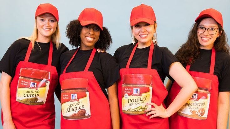 four women dressed in red aprons with different spices on the front and red hats