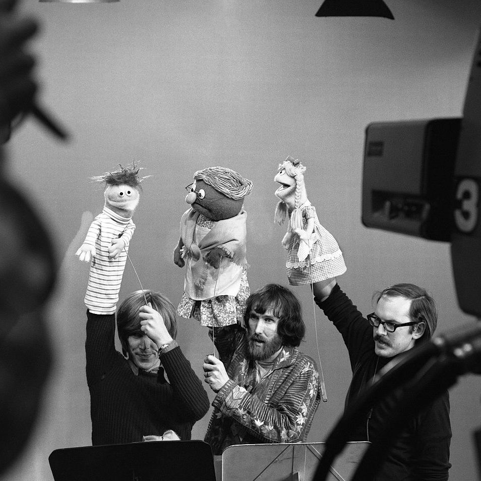 daniel seagren, jim henson, and frank oz each hold a muppet in one hand with their arm raised over their heads, a tv camera looks on from the foreground