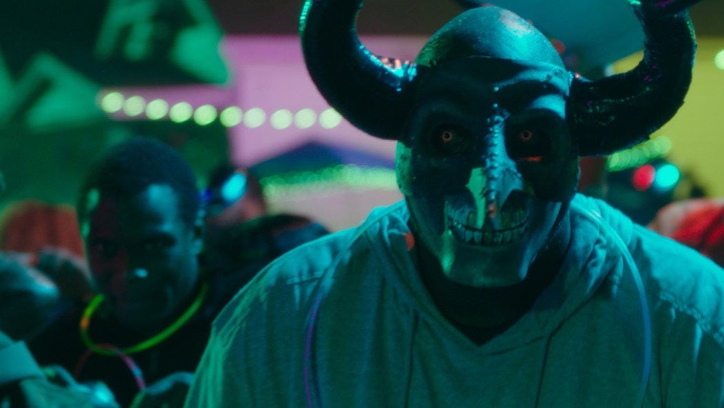 a man wears a mask with giant horns and glowing eyes in a scene from the first purge, the fourth film if you want to watch the purge movies in order