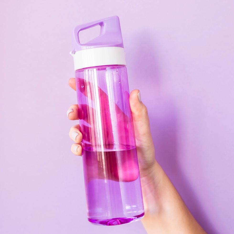 hand holding purple plastic water bottle against purple background