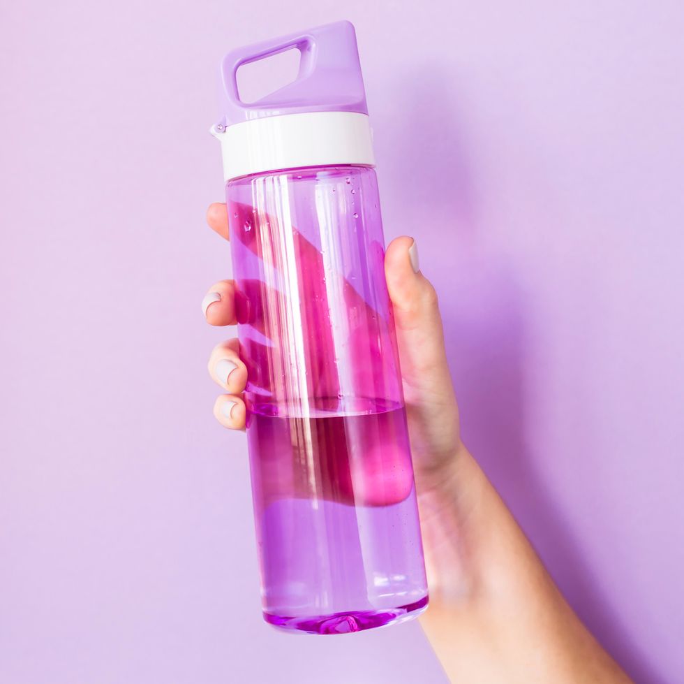 hand holding purple plastic water bottle against purple background