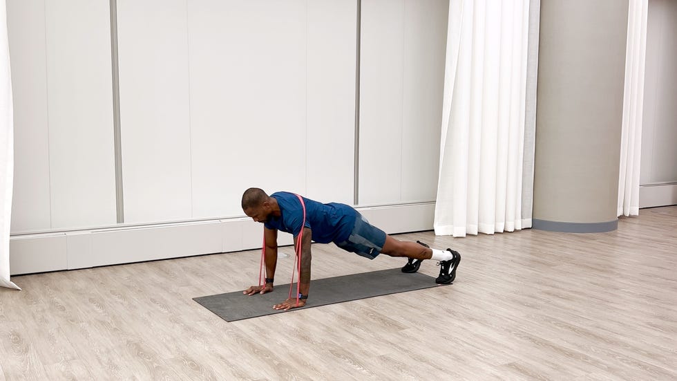 man performing push up exercise with a resistance band on a mat in a gymlike setting.