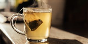 putting tea bag into glass cup full of hot water