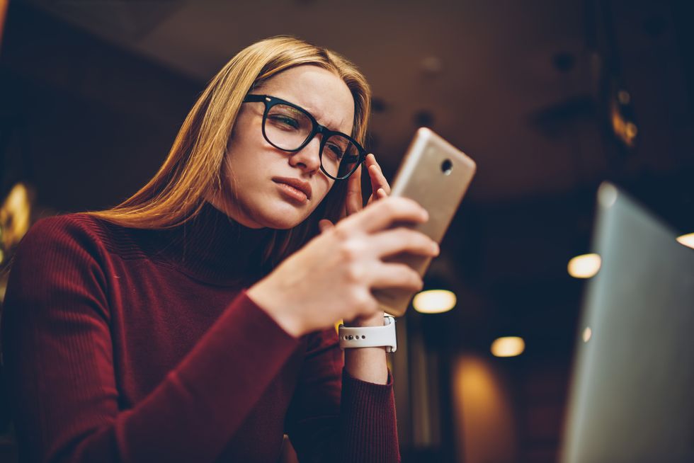 puzzled woman in spectacles for provide eyes protection reading bad news about internet connection via text message from operator on cellular phone, hipster girl dialing number and feeling headache