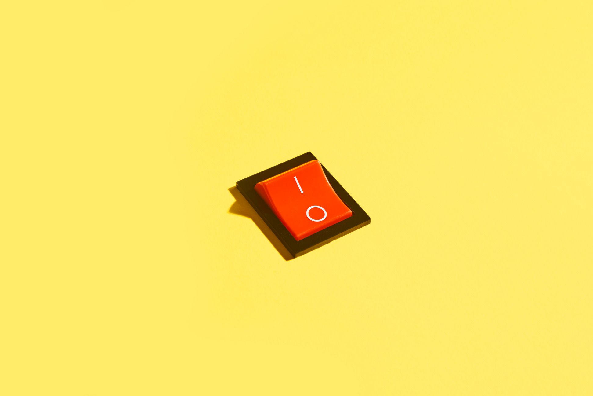 high angle view of a red rocker switch with power on and power off symbols printed in white, switched in the power off position on yellow background