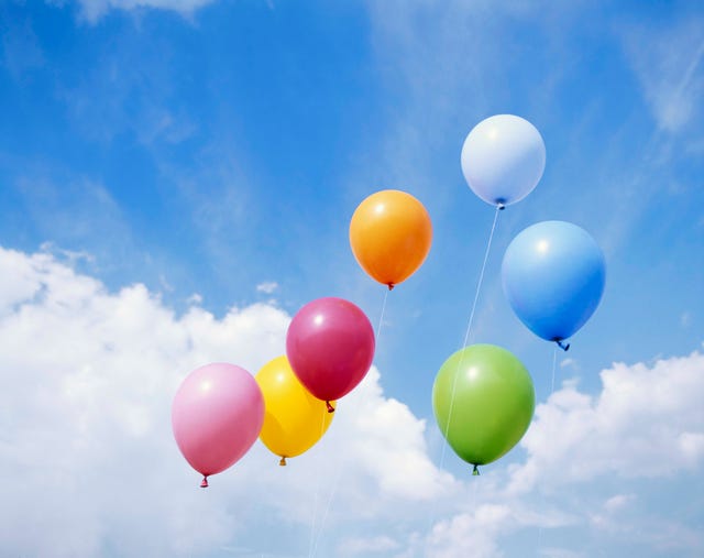 colorful balloons floating through blue, cloudy sky