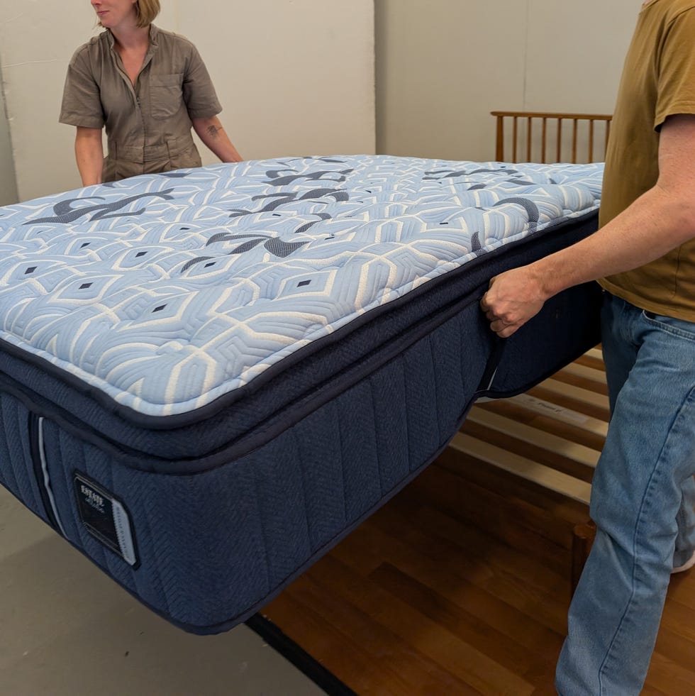 best cooling mattress - testing image two people setting up a blue mattress on a wooden bed frame, good housekeeping's best cooling mattress