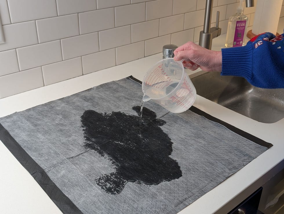 pouring a mix of water and vinegar onto a black puppy pee pad at the good housekeeping institute