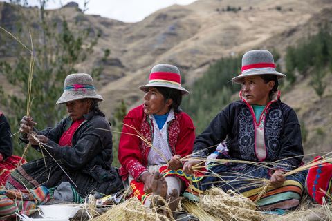 Kleurrijk geklede Quechuavrouwen vlechten het touw bovenaan de kloof