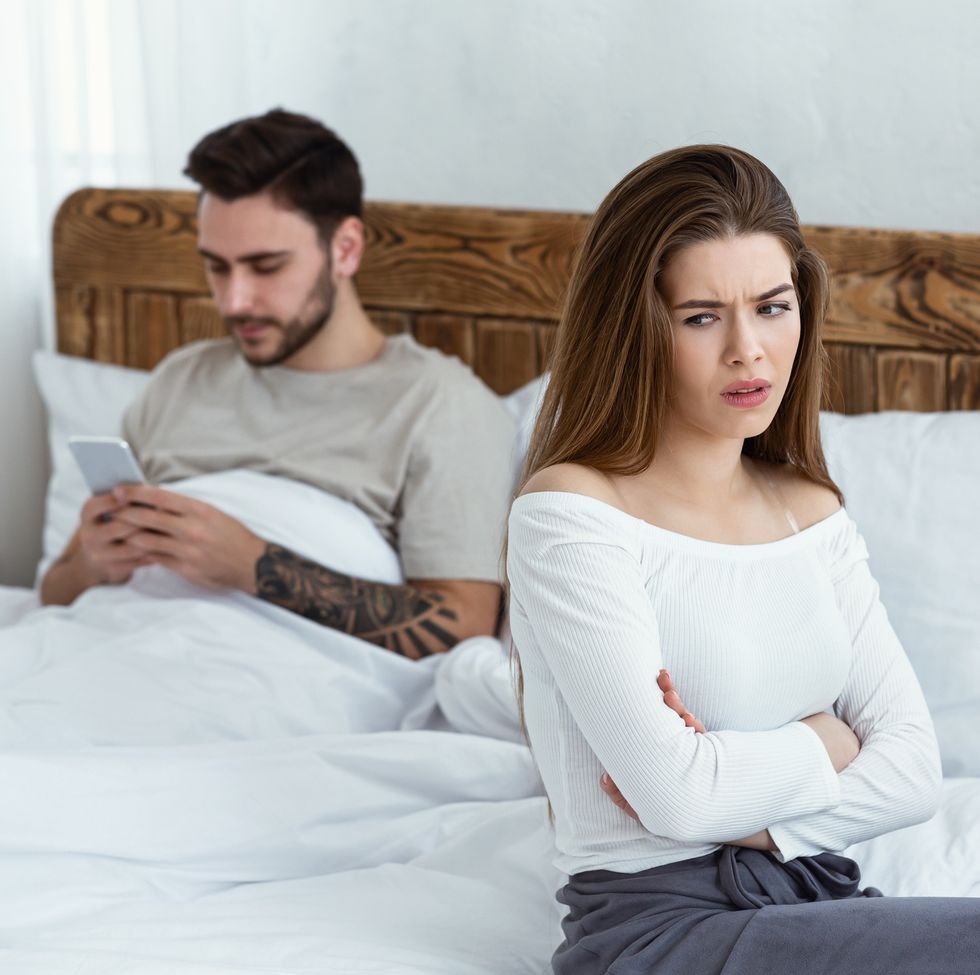 quarrel and jealousy guy in bed chatting on smartphone, offended girl crossed her arms