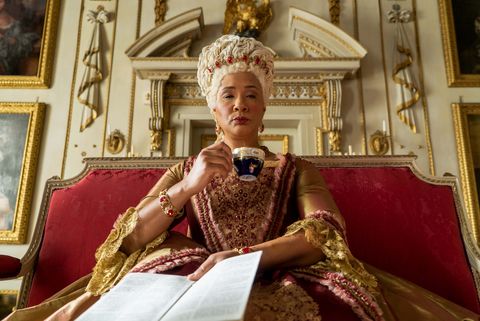 bridgerton golda rosheuvel as queen charlotte sitting and drinking tea in gold and rose dress in episode 105 of bridgerton