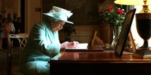 queen elizabeth signing a letter during a visit