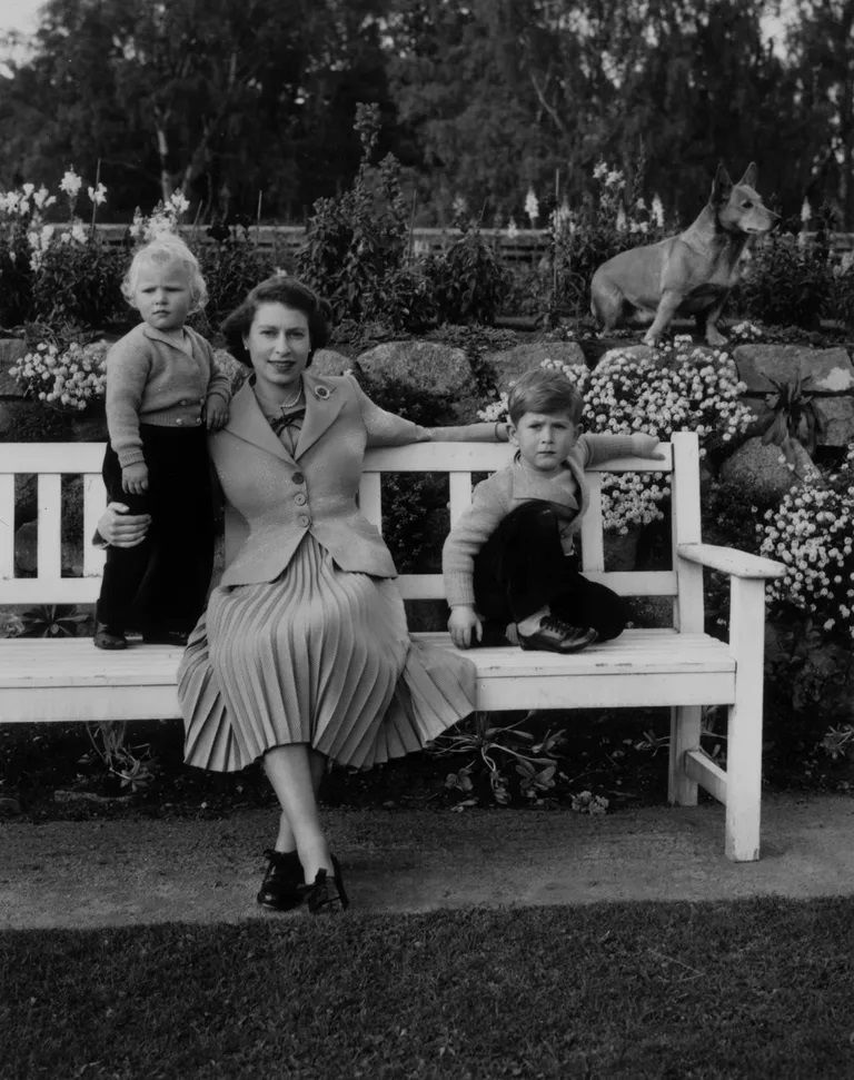 queen elizabeth sitting with her children, charles and anne and a royal corgi