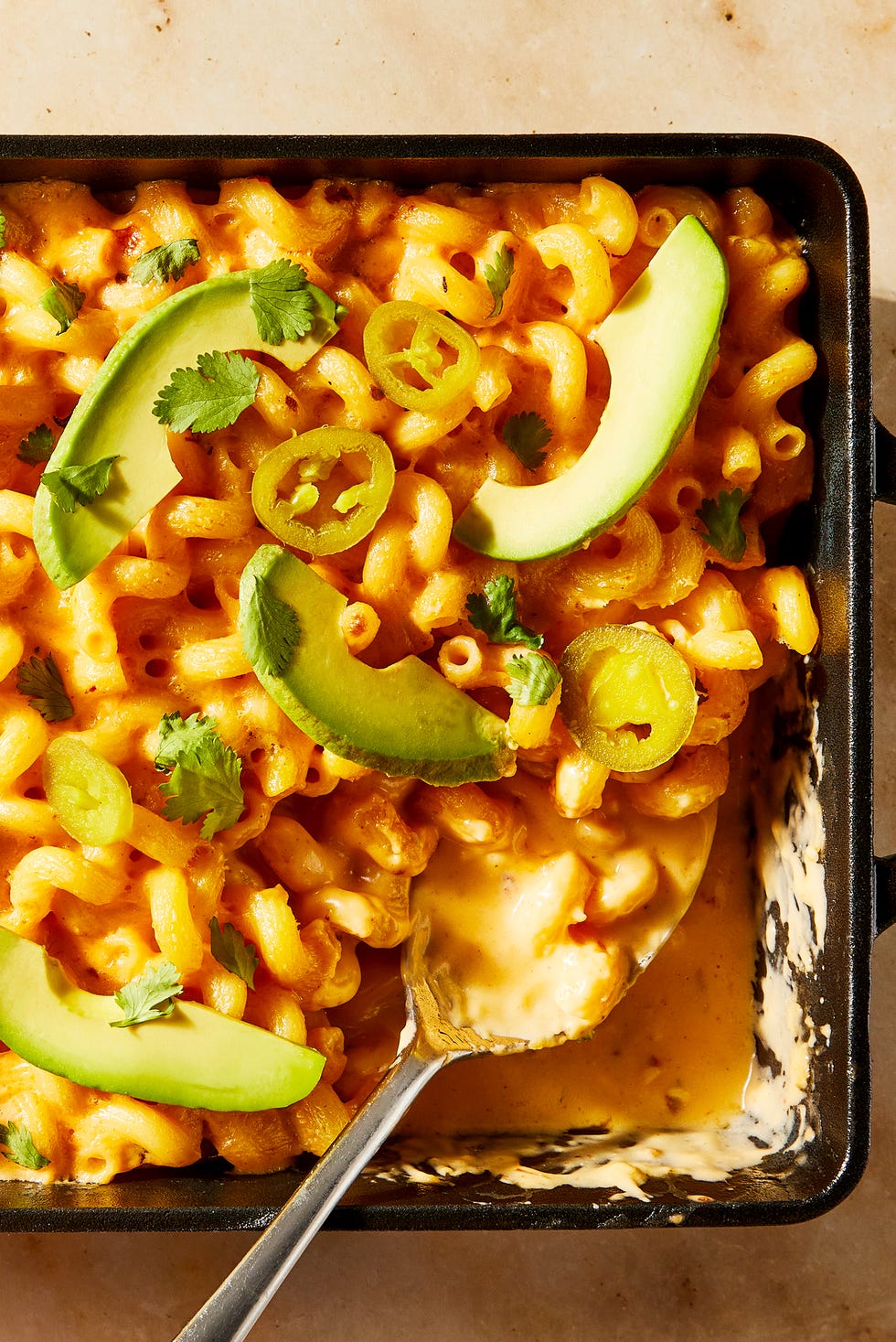 Queso Mac & Cheese Macaroni and cheese topped with sliced avocado and jalapeños