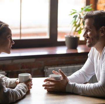 side view of couple sitting at a table in front of a window talking and drinking tea or coffee talking and smiling