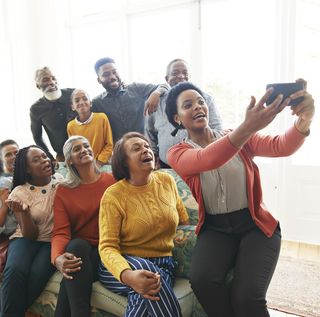friends are family quotes  woman holding her phone to take a selfie with her family and friends on a couch
