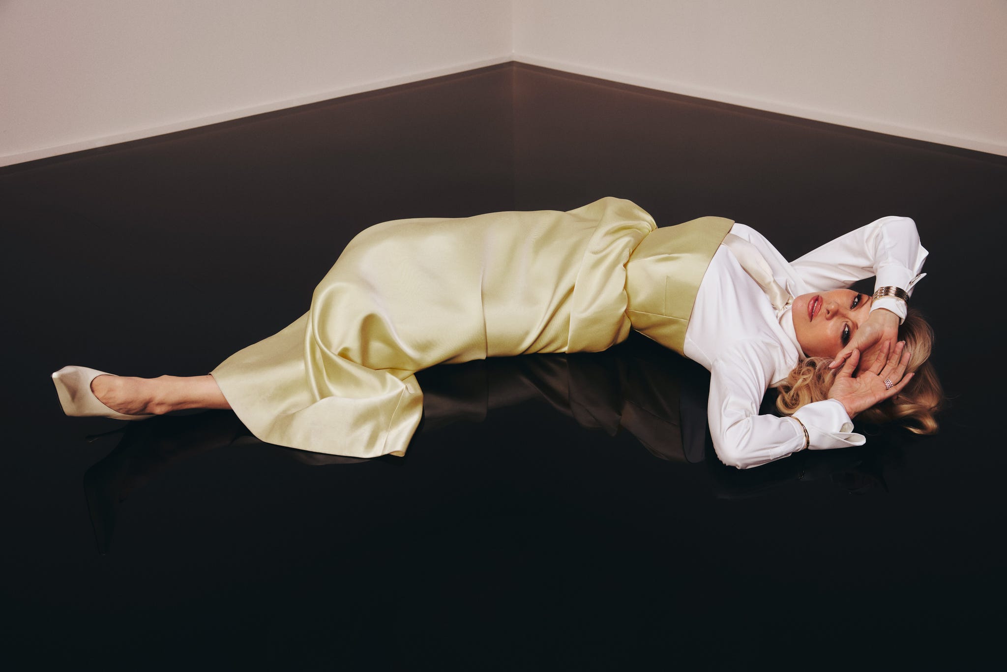 A person lying on a reflective surface wearing a yellow skirt and white blouse