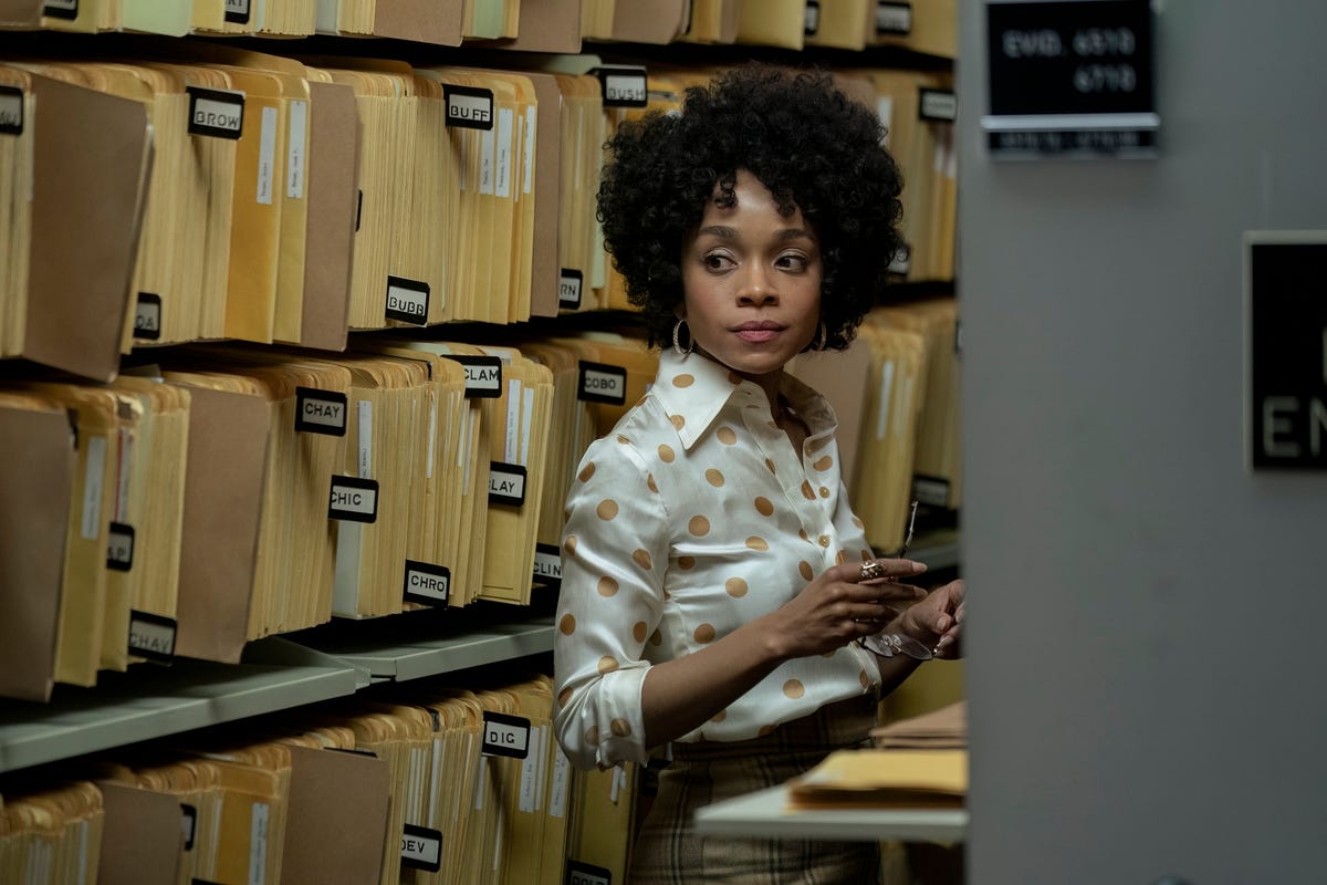 a woman stands among file folders on shelves as she looks to the right