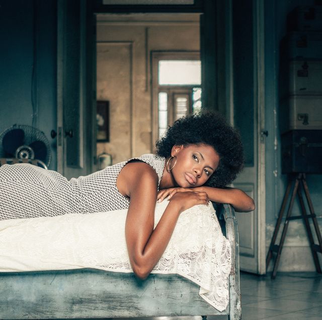 zwarte vrouw ligt op bed in grijze jurk in blauwe kamer
