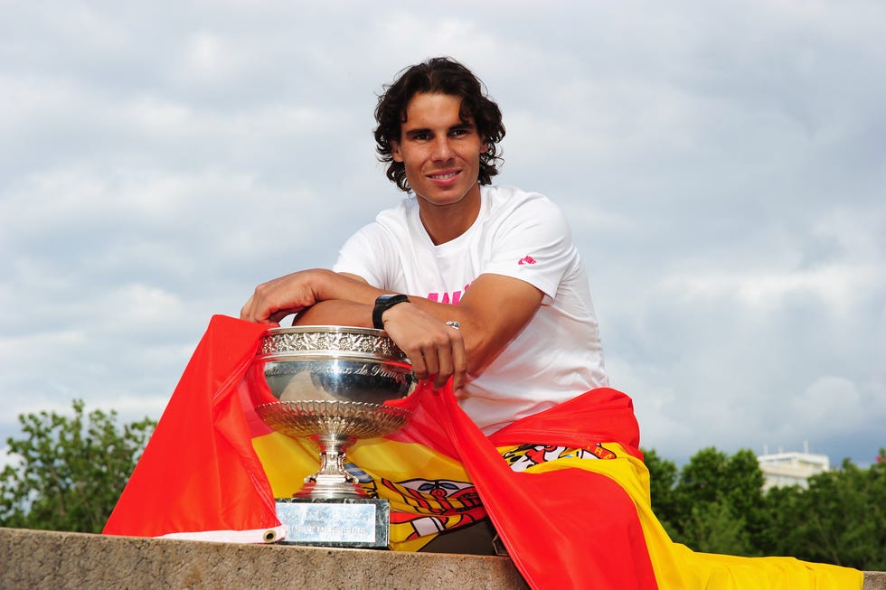 rafael nadal resting his hands on a trophy with a spanish flag draped over him
