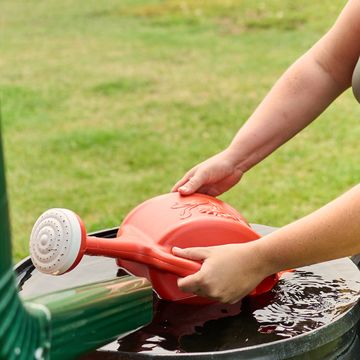 woman filling watering can with water from a rain barrel