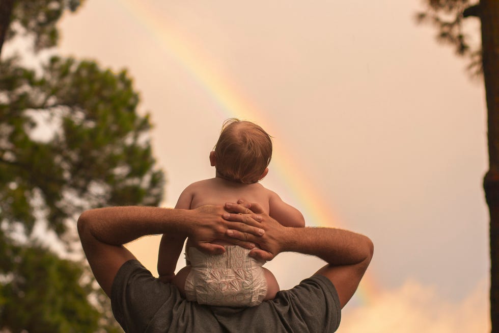 rear view father carrying son on shoulders while looking at rainbow