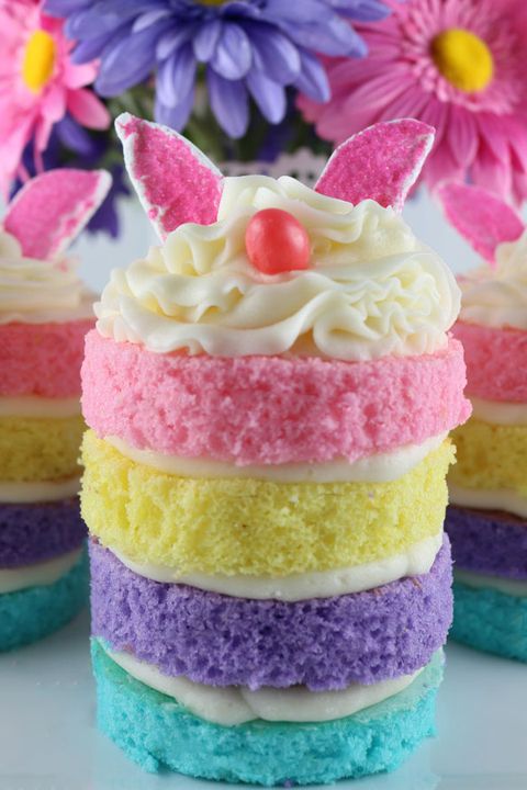 mini cake with four pastel colored layers and frosting piped on top with ears and a nose like a bunny