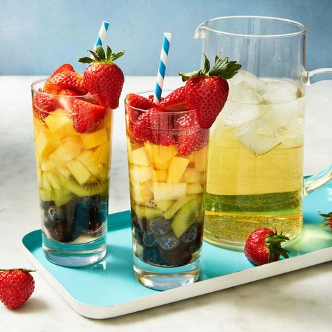 rainbow sangria in a glass with a pitcher next to it
