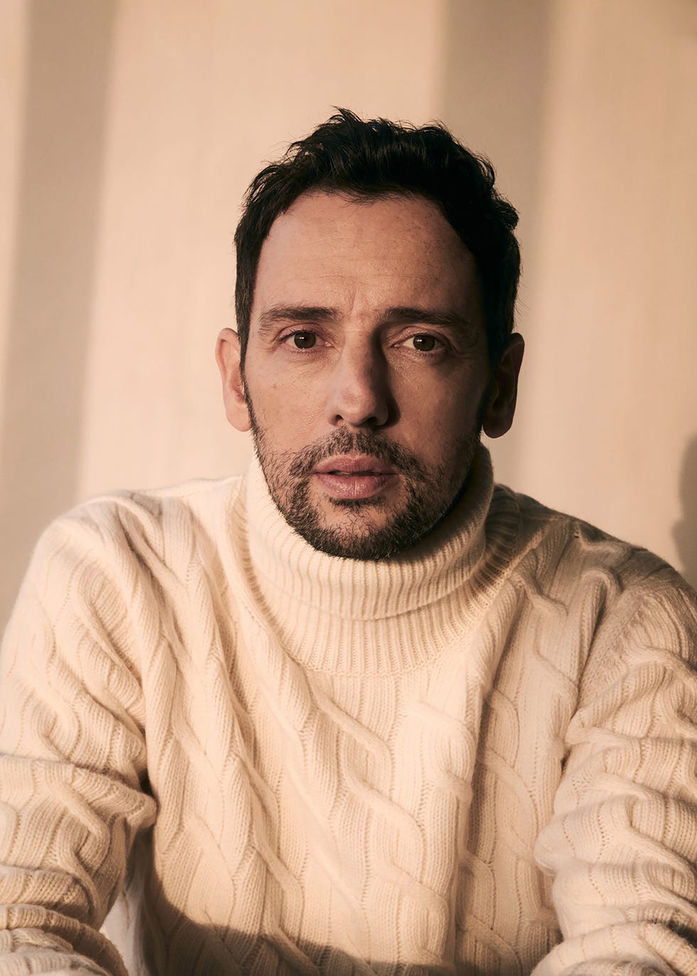 a person wearing a knitted sweater is seated against a neutral background