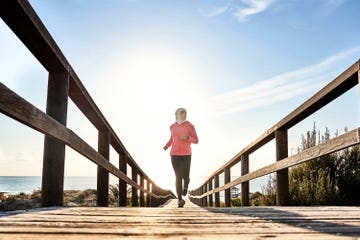 a person jogging on a wooden pathway towards the beach under bright sunlight