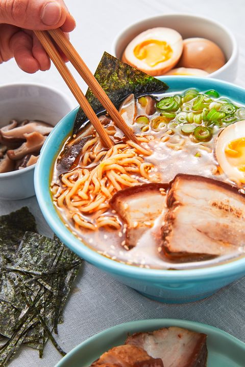 homemade ramen topped with pork, a soft boiled egg, scallions, and nori in a blue bowl surrounded by ingredients