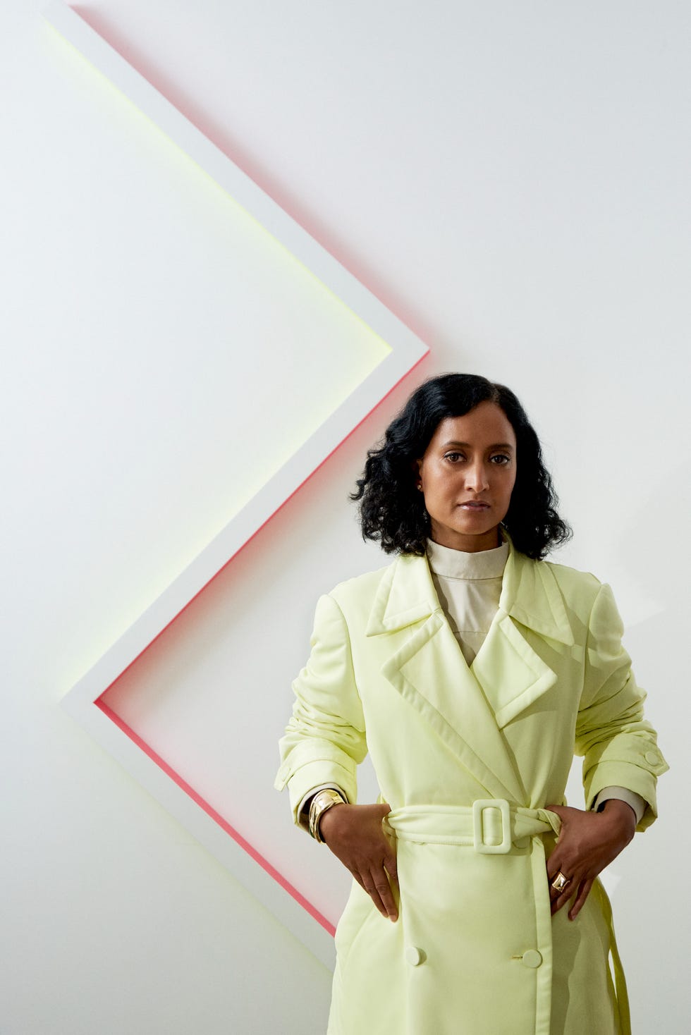 a figure is positioned centrally wearing a light yellow trench coat styled with a belt