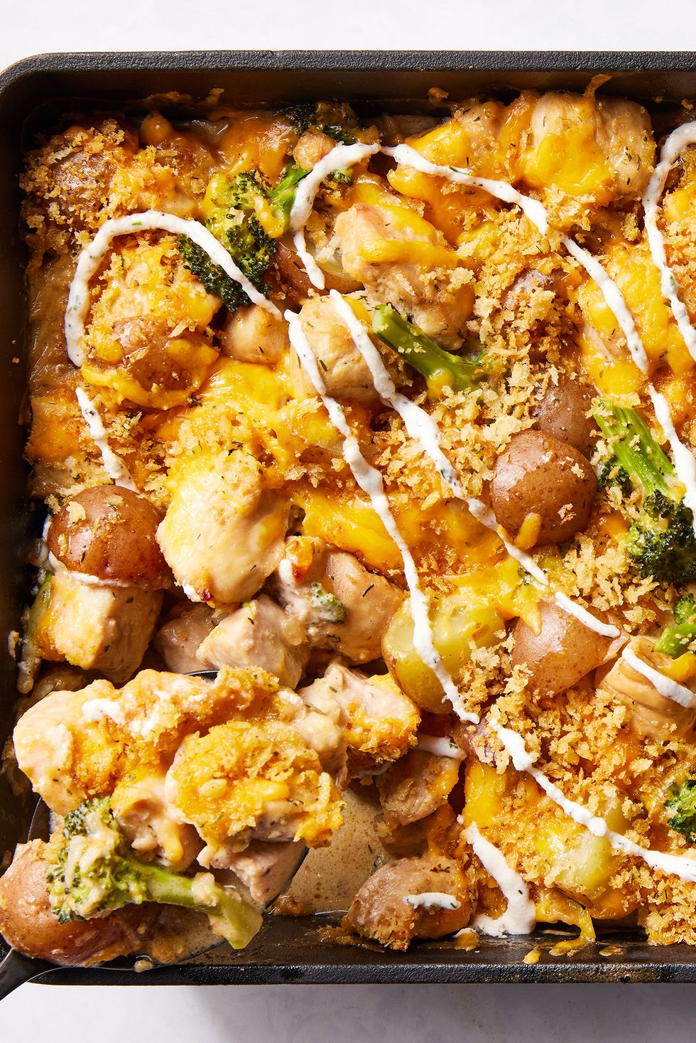 chicken with potatoes, broccoli, melted cheese, and drizzled with ranch in a casserole dish