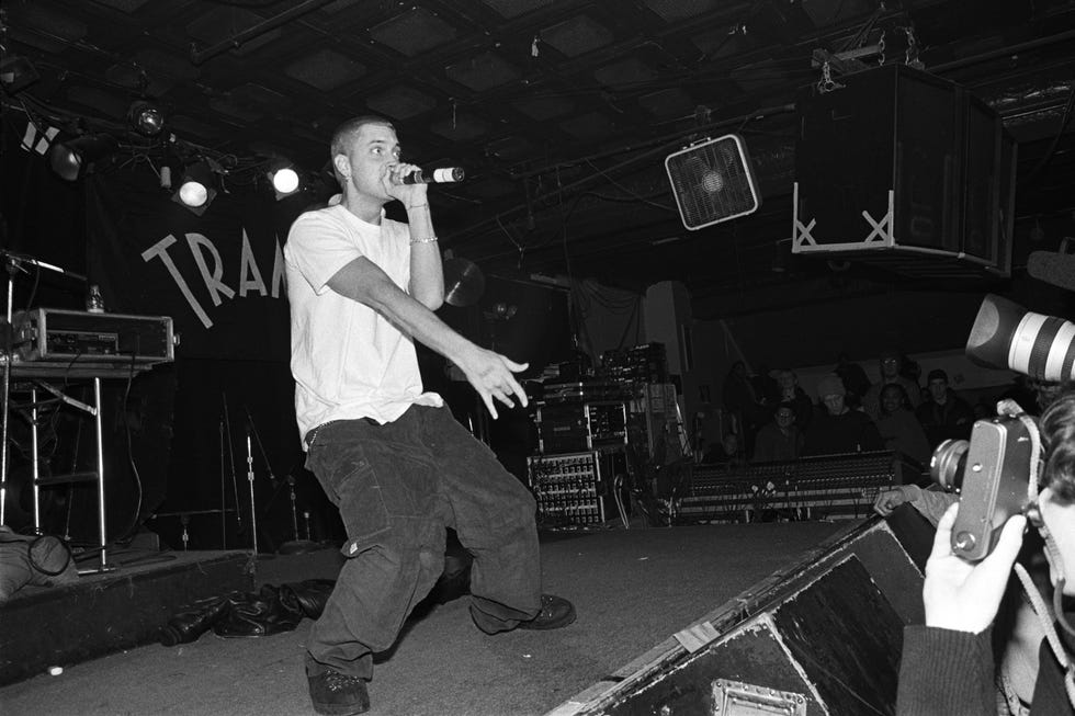 eminem sings into a microphone he holds as he stands on a stage in a tshirt and baggy pants