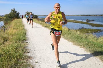a runner wearing a yellow tank top and black shorts on a path along a water body