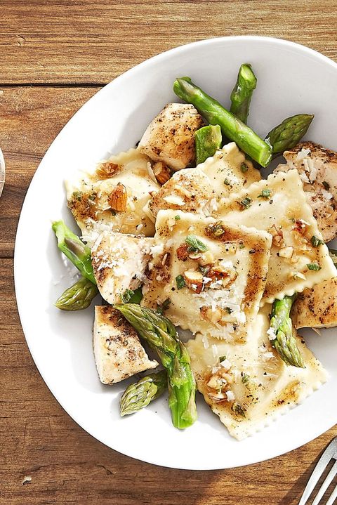 ravioli pasta served on a white plate with chicken chunks, asparagus, and a browned butter sauce